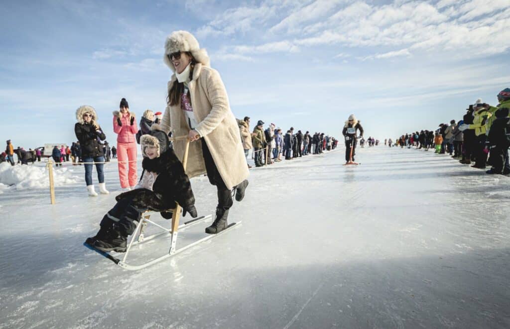 Ema ja laps jäätunud Peipsi järve peal Kolkja kelguga kelgutamas, ümber on inimesi