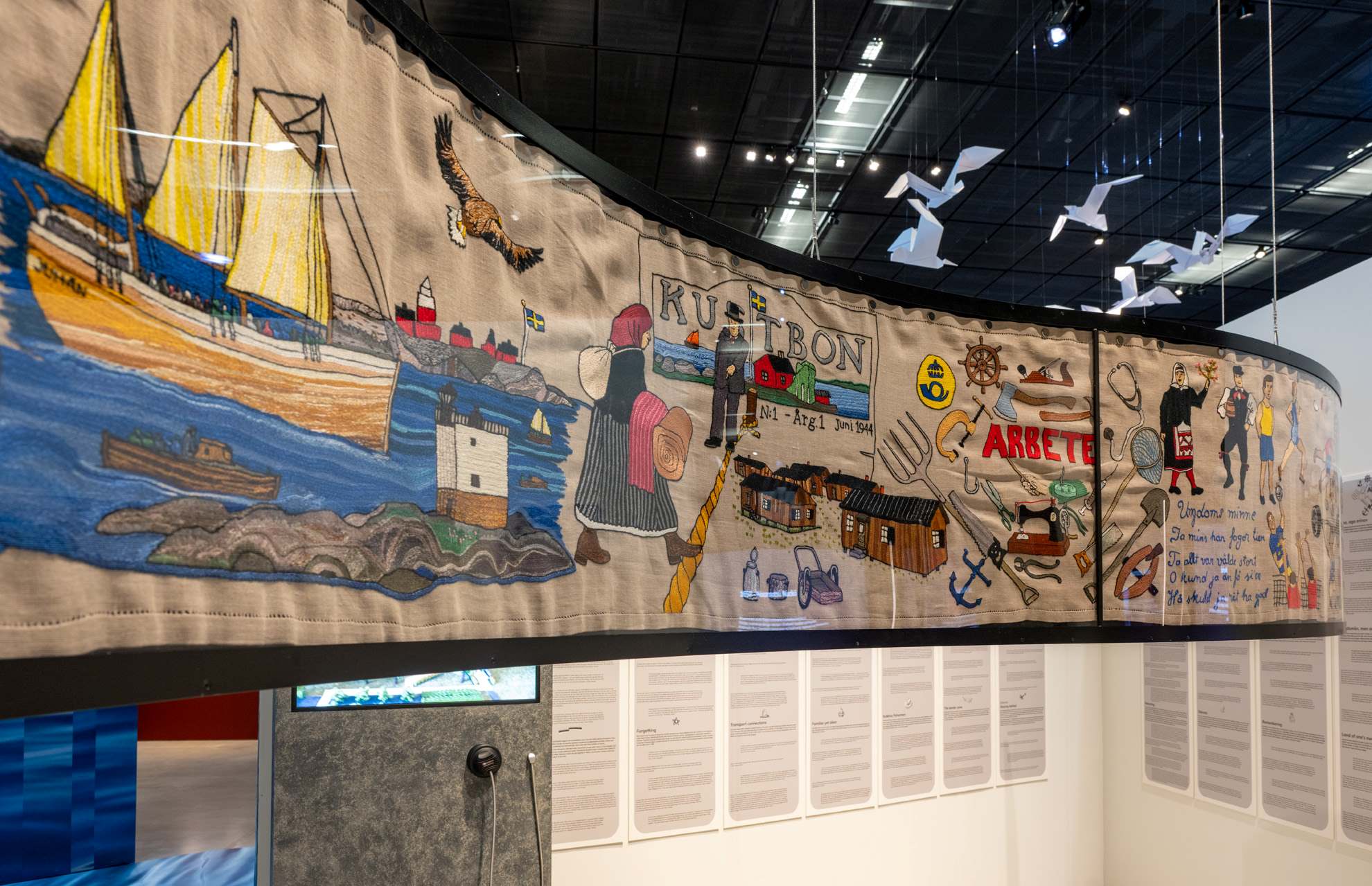 Eesti Rahva Muuseumi aastakonverentsi näitusel eksponeeritud rannarootslaste elu kujutav tikitud seinavaip paatide, inimeste ja tööriistadega