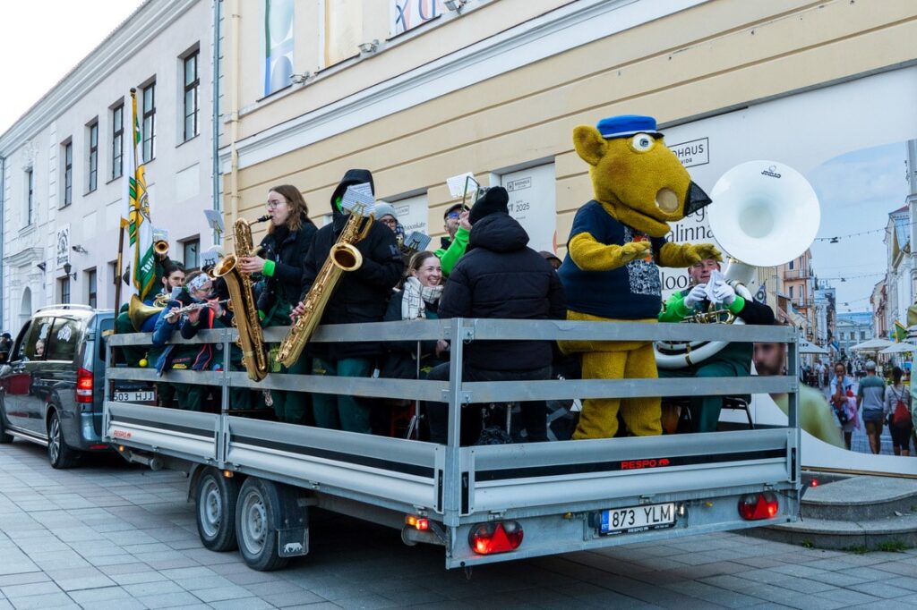 Tudengipäevade rongkäigu osalejad ja puhkpillimängijad sõidavad haagisel mööda Tartu kesklinna tänavat.
