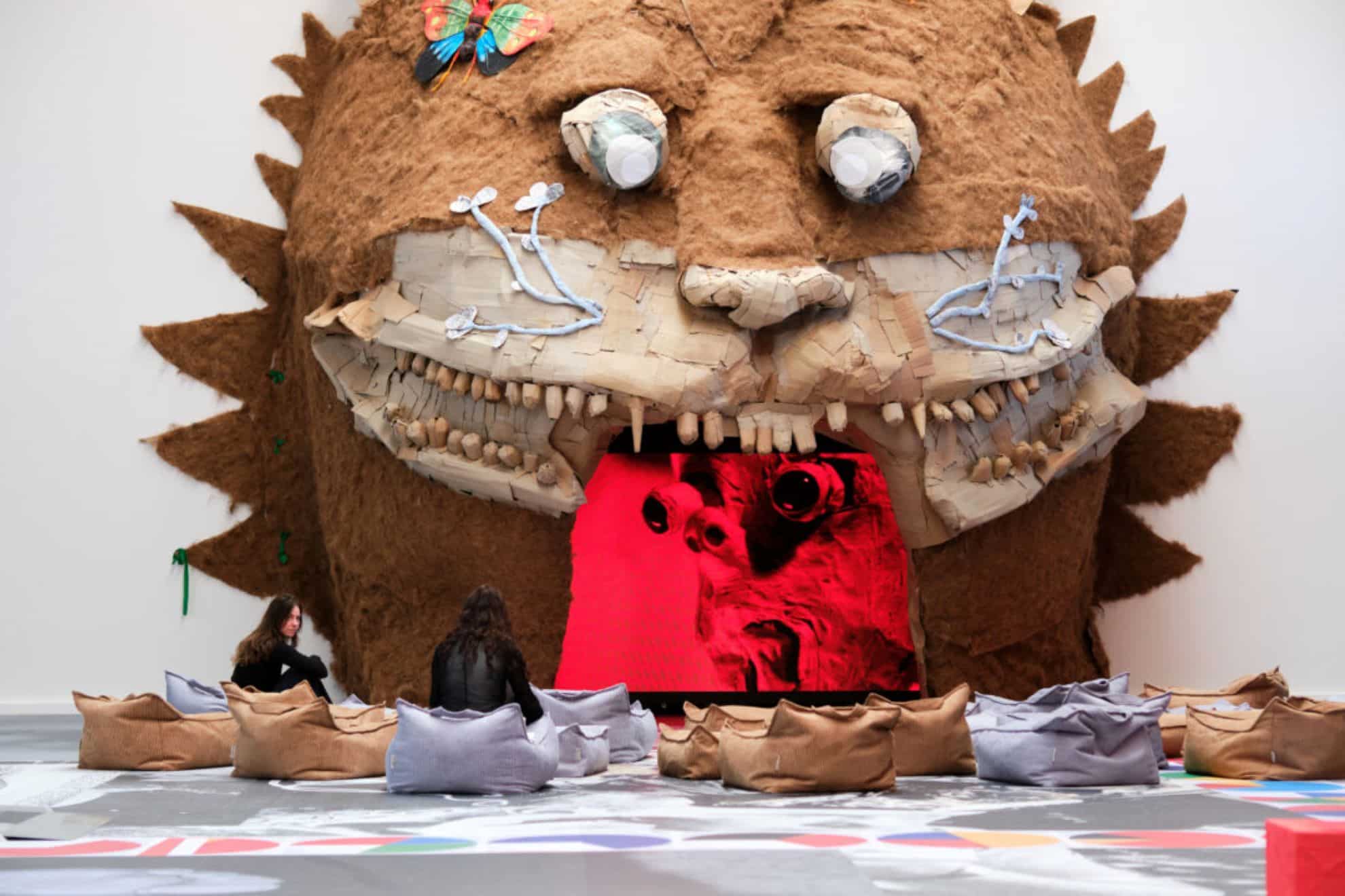 Kaks inimest istuvad patjadel ja vaatavad suurt kunstinstallatsiooni – karvast, hiiglaslikku looma meenutavat pead, mille avatud suus jookseb punaka valgusega video