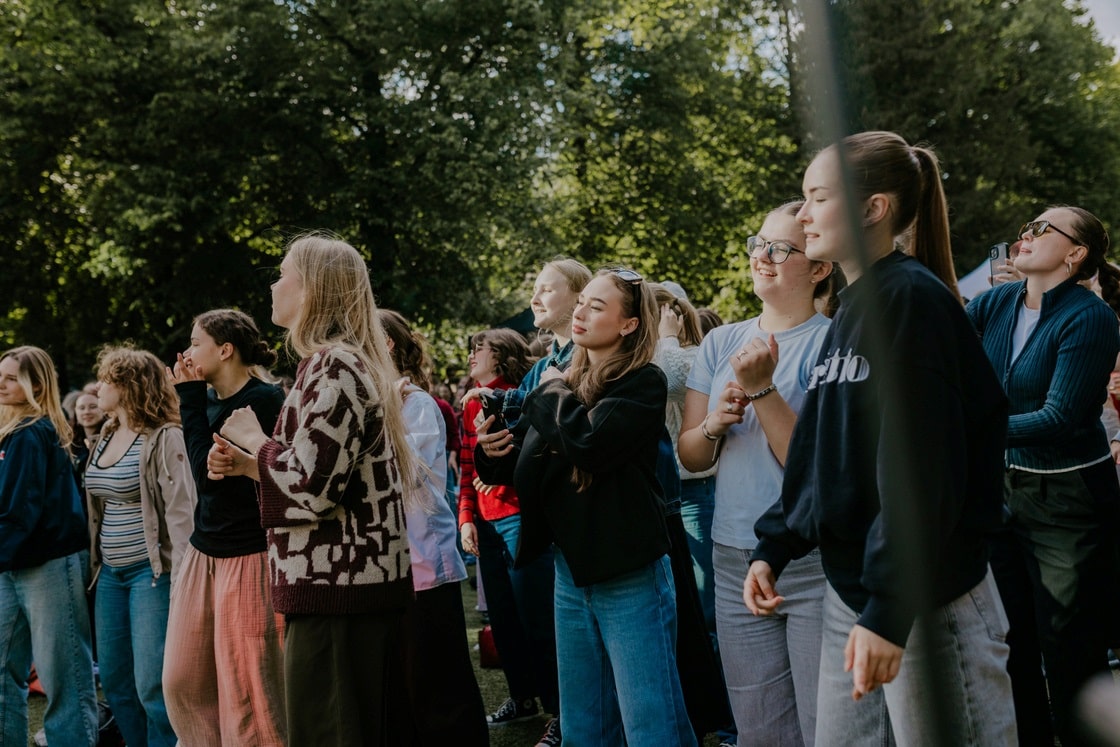 Noored seisavad päikeselisel päeval Tartu linna pargis ja jälgivad ühiselt väliüritust.