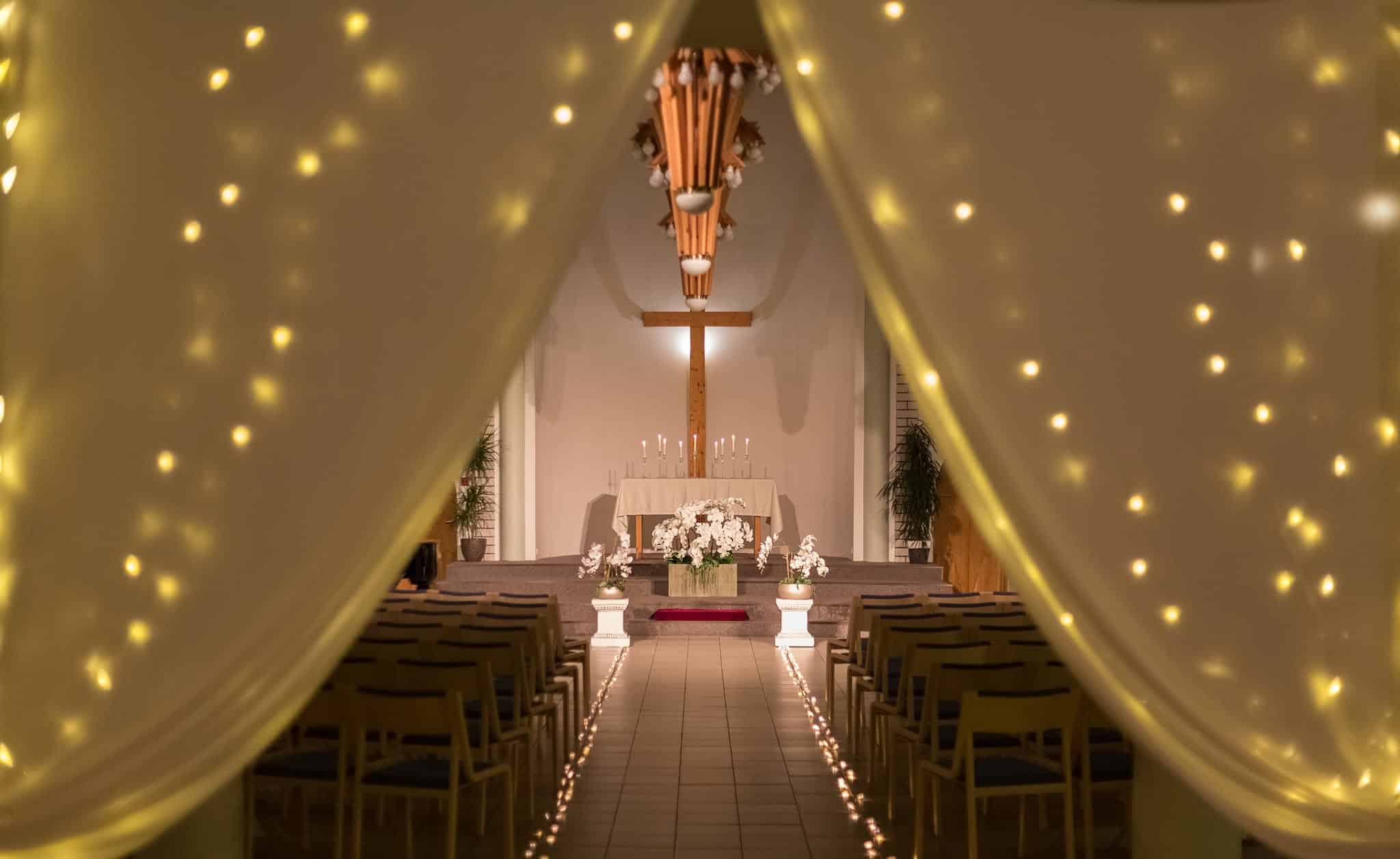 Pidulikult valgustatud Tartu Salemi kiriku saal altari, risti ja küünaldega Väikese Kirikumuusika Festivali kontserdi eel.