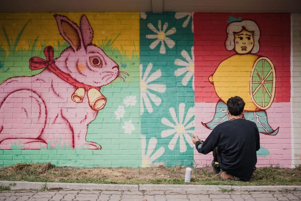Street artist painting a colourful mural on a street in Tartu; the mural depicts a person and a rabbit