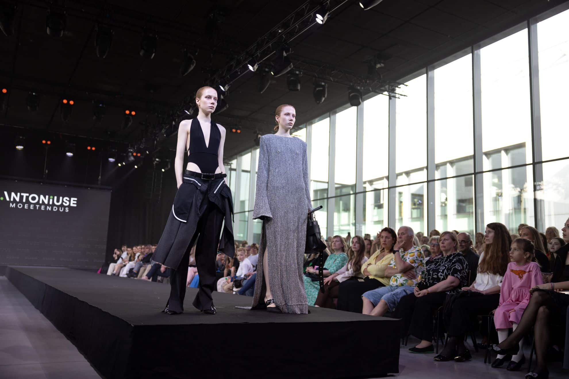Kaks modelli kõnnivad Estonian Fashion Festivali moeetendusel laval Tartus Eesti Rahva Muuseumis, samal ajal kui publik jälgib etendust saalist.