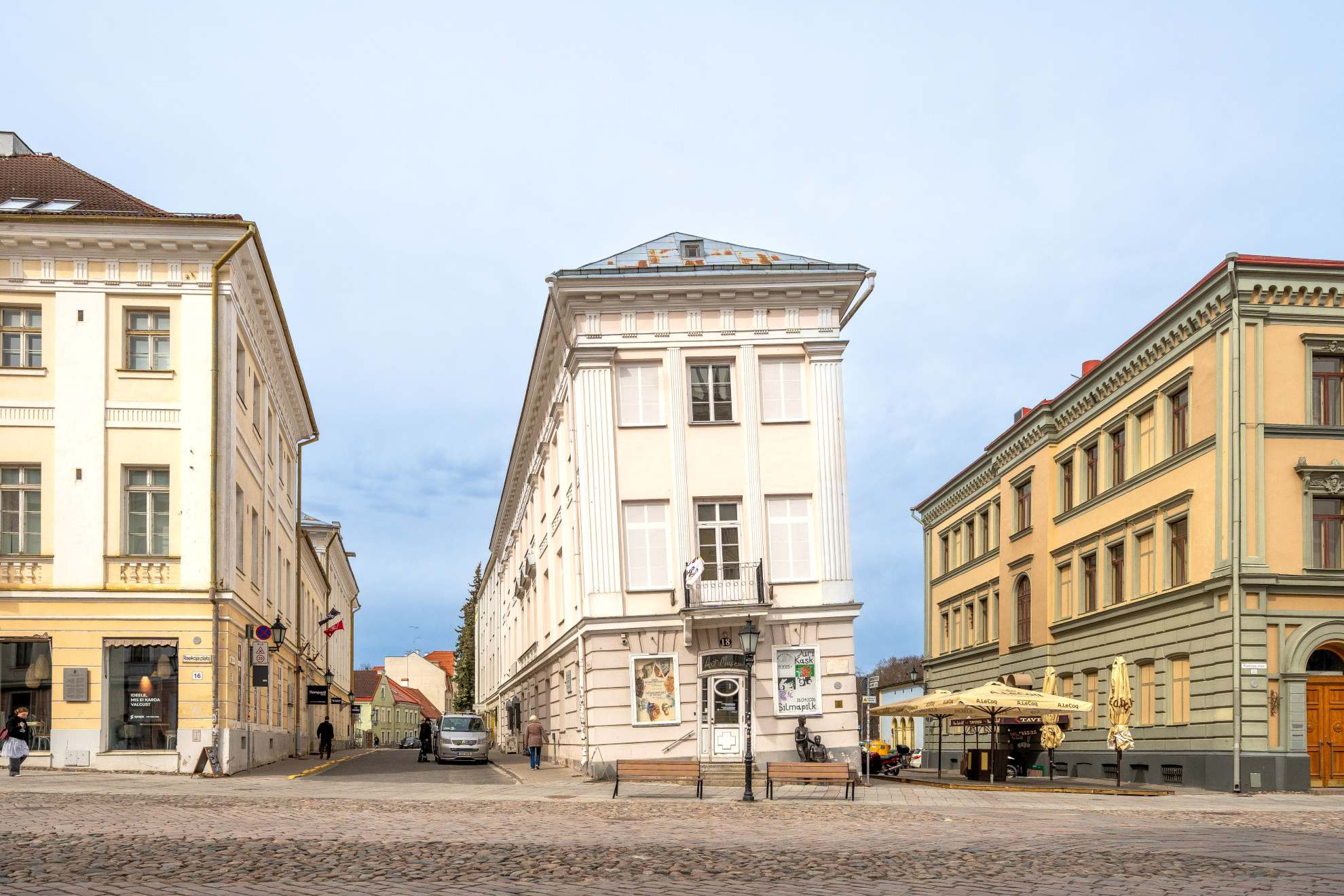 Tartu Kunstimuuseumi viltune maja Raekoja platsi ääres, taustal ajaloolised hooned ja munakivisillutisega tänav.