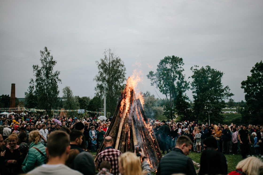 Rahvas on kogunenud suure jaanilõkke ümber Tartu linnas Eesti Rahva Muuseumi kõrval, mille leegid tõusevad pilvise taeva taustal.