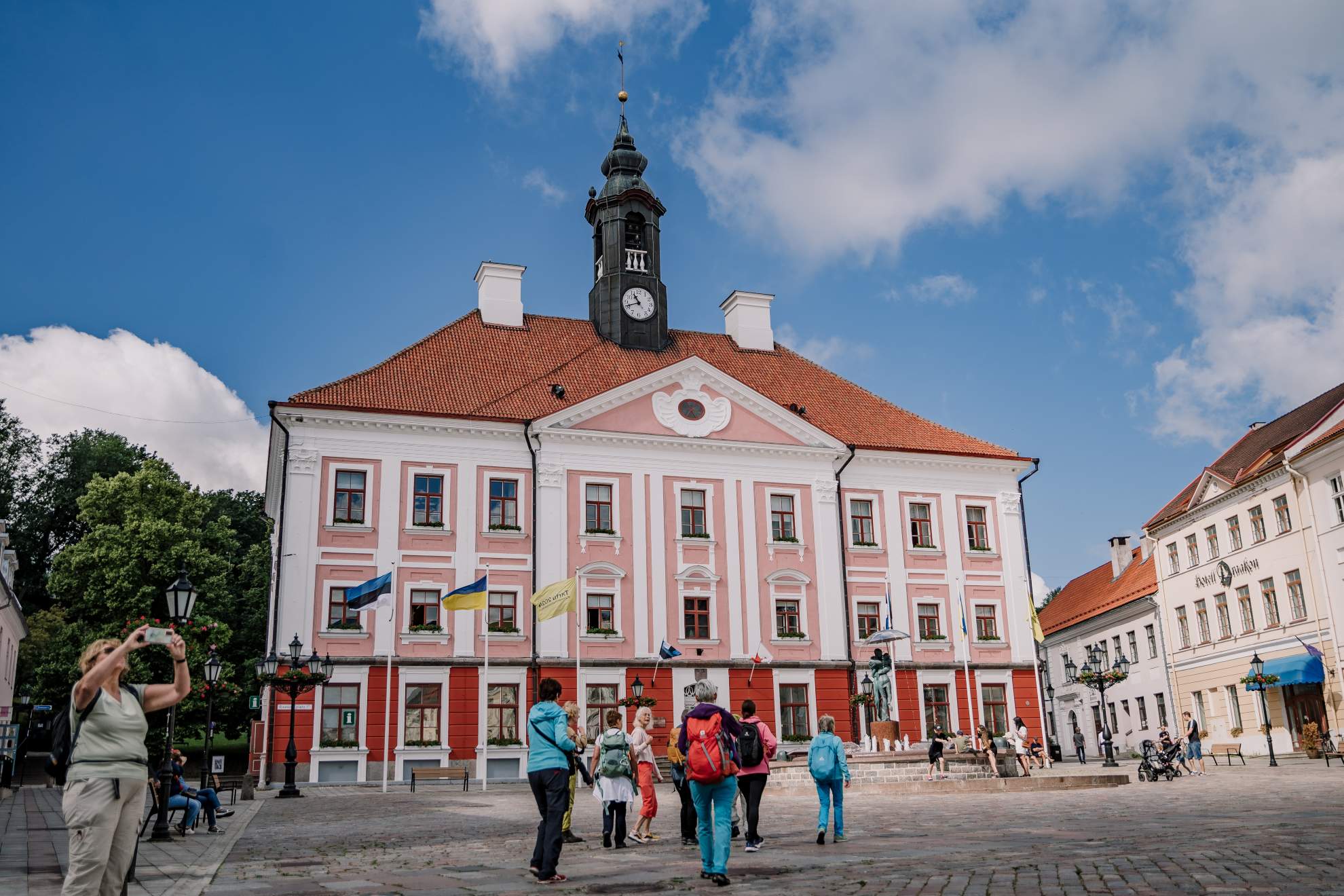 Tartu Raekoda ja Raekoja plats suvisel päeval, väljakul jalutavad inimesed ja turistid.