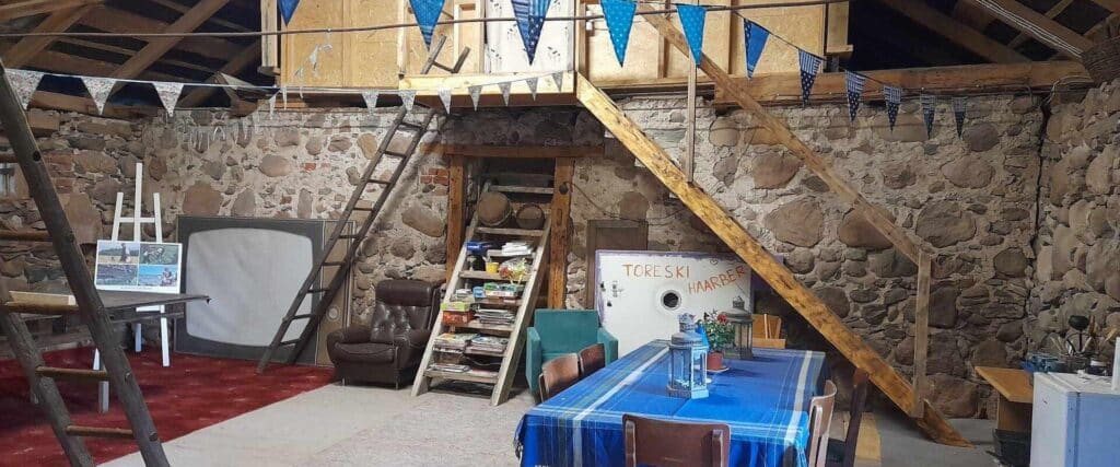 Toreski Farm's stable interior features stone walls, a dining table, and a cozy seating area.