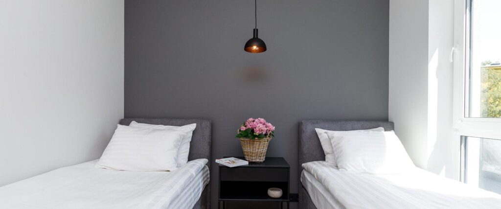 Modern double room at Rare Apartments accommodation with a grey accent wall and a basket of flowers.